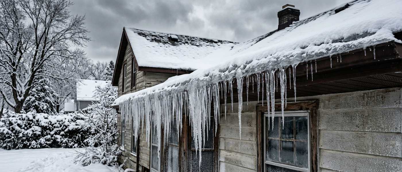 Ice ridge and long icicles along the snowy roof edge of an older house